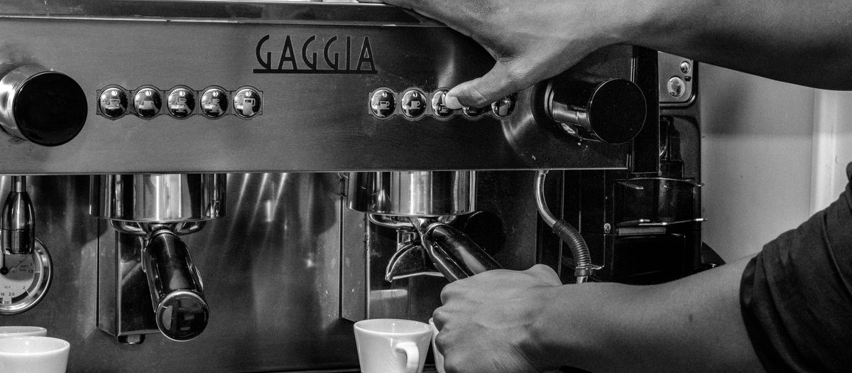Black and white photo of a barista operating a Gaggia espresso machine in a café.